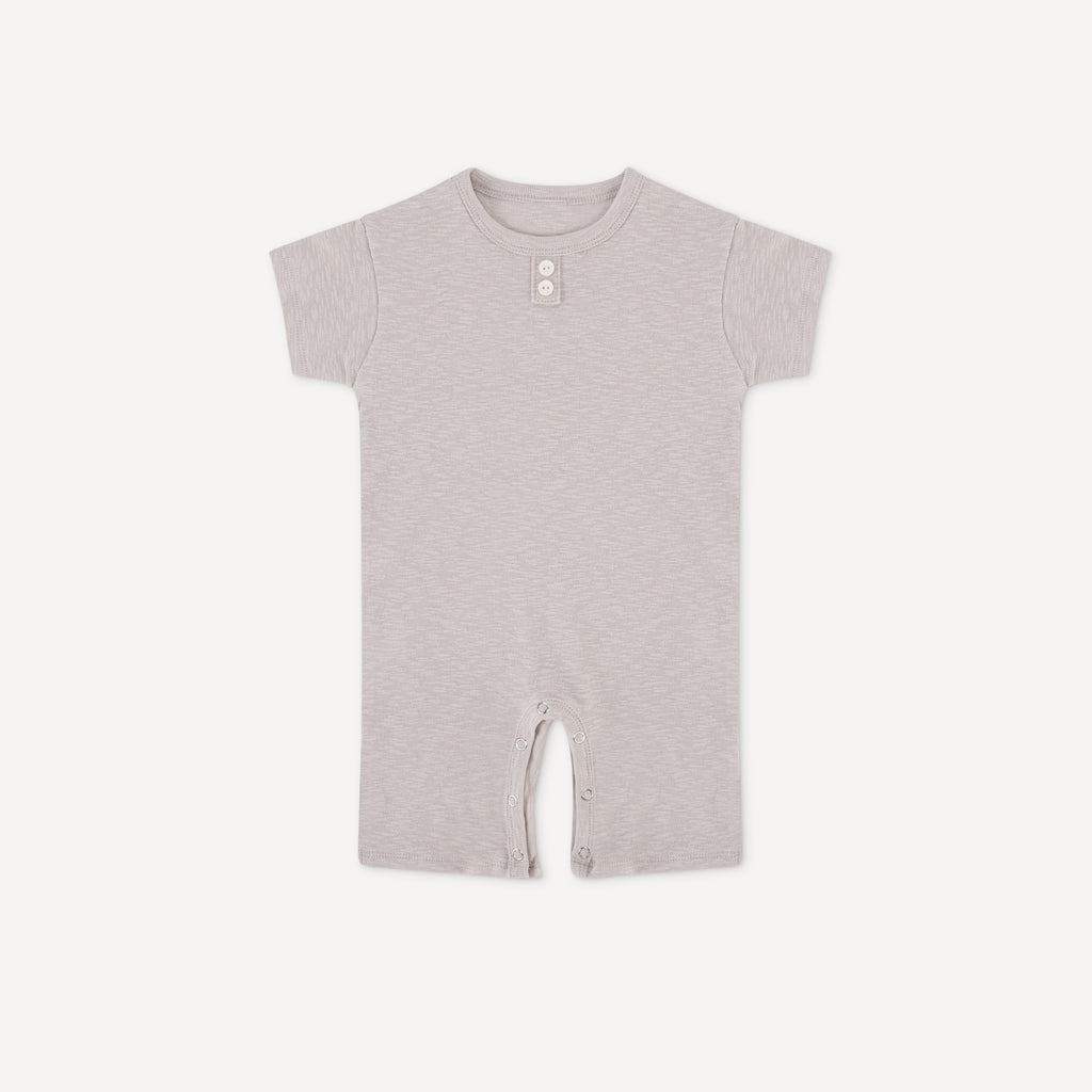 A gray-colored Coco Onesie by Apples and Bananas, designed with short sleeves, a simple button at the neck, and convenient snap closures at the bottom.